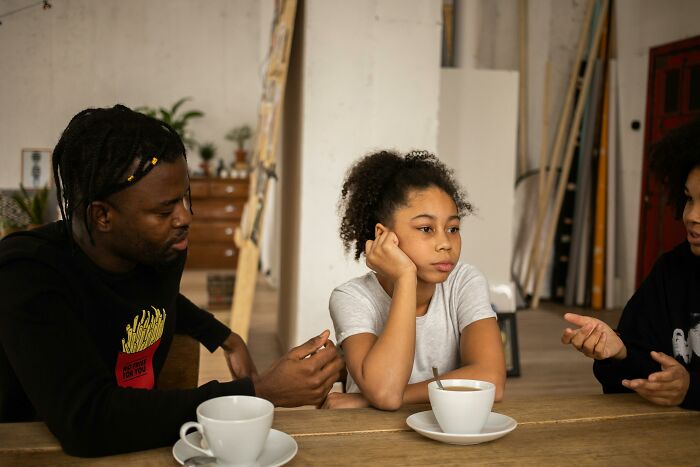 A young girl looks bored at a table with two adults, representing kids who realize parents never wanted them.