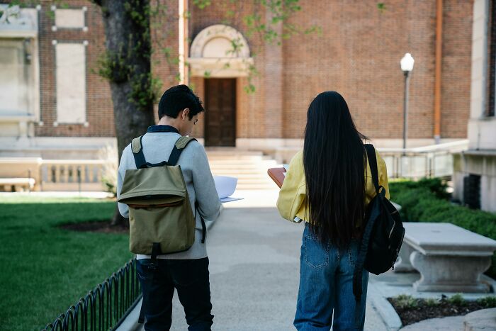Two college freshmen with backpacks walk on a path, possibly heading to a challenging quiz.