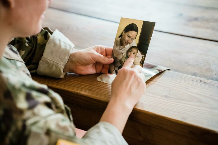 Person in uniform holding old photo of mother and child reflecting on past