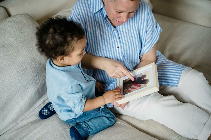 Mother showing photo album to toddler on sofa