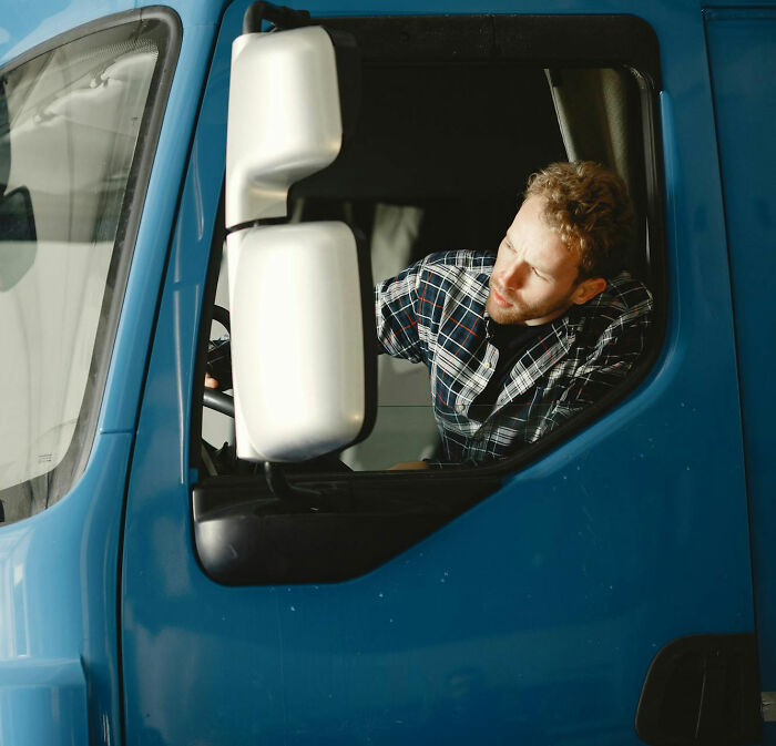 Truck driver checking side mirror in blue truck cab on a challenging road