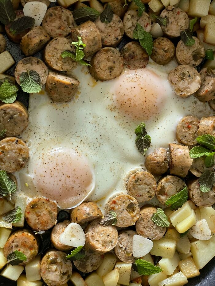 Poverty meals with eggs, sausage pieces, potatoes, and fresh herbs in a skillet