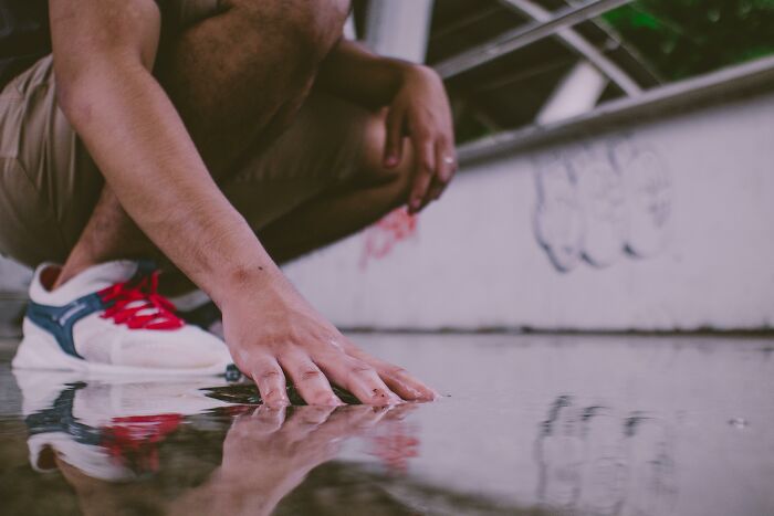 Person crouched down touching wet surface on ground near graffiti wall