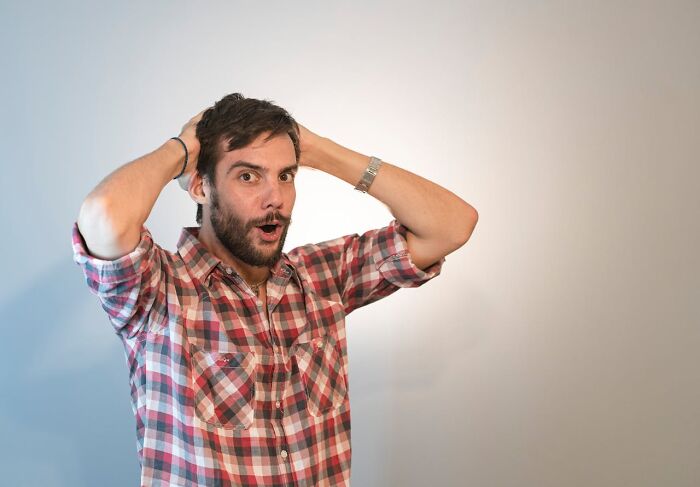 Man in plaid shirt looking surprised with hands on head, laziness saving people concept