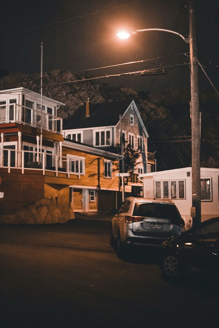 Streetlight illuminating quiet residential street at night with parked cars