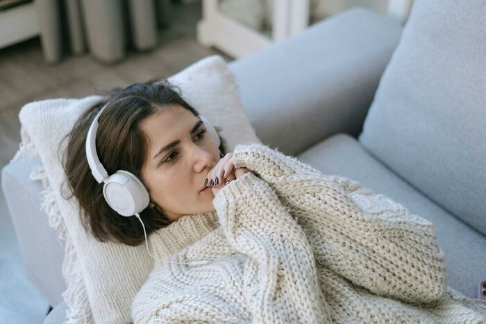Woman wearing headphones, lying thoughtful in sweater