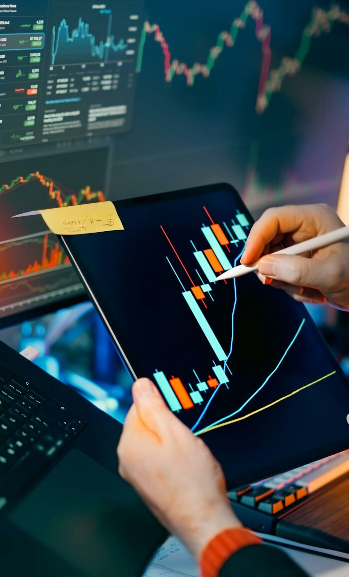 Hands analyze stock market data on a tablet with a stylus, displaying charts. A screen with graphs is in the background. Immoral acts impact lives.