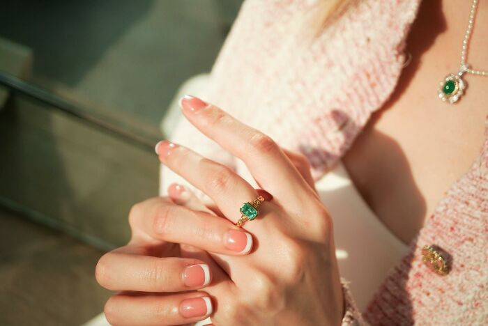 Close-up of a woman's hands with French manicures, wearing a gold emerald ring, evoking a glitch in the matrix.