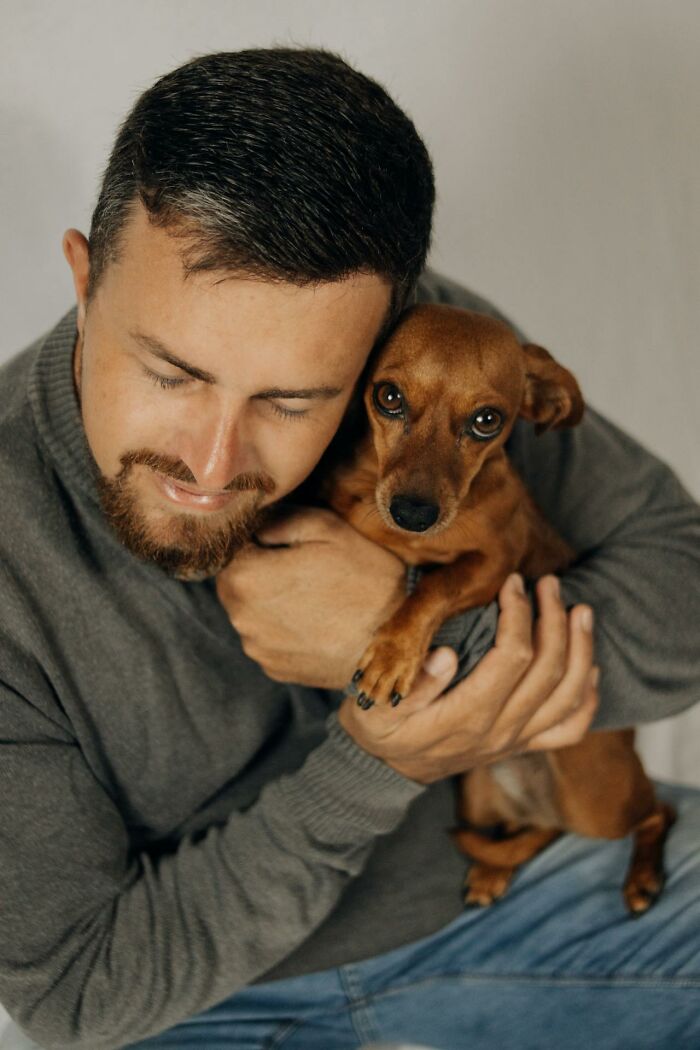 Man hugging a small brown dog close to his face