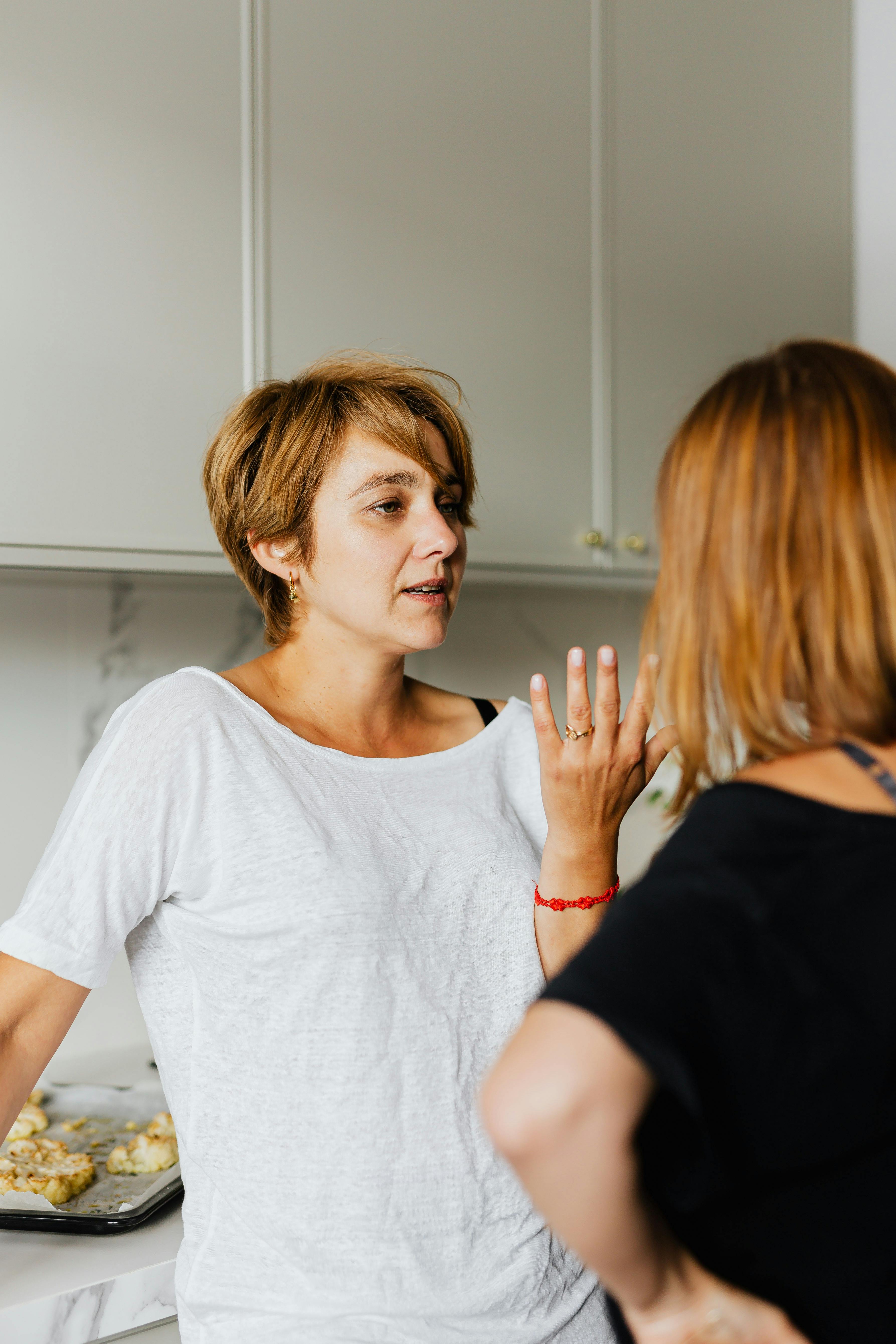Woman in white shirt having intense conversation with another woman in kitchen Woman in white shirt having intense conversation with another woman in kitchen