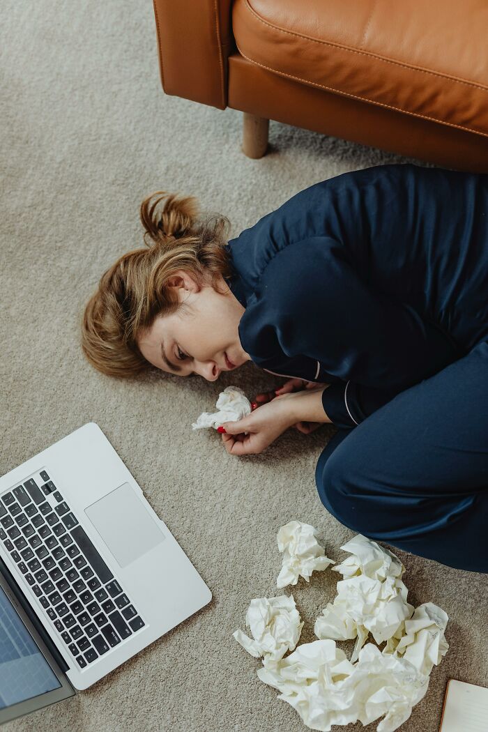 Woman lying on the floor surrounded by crumpled paper, frustrated with Gen Z. Laptop nearby.