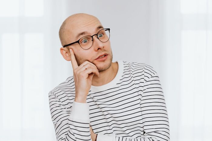 Thoughtful bald man wearing glasses and striped shirt looking aside