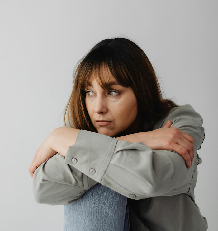 Sad woman sitting indoors hugging knees thinking about cult escape moment