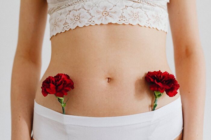 Close up of woman with red flowers tucked in waistband of white pants