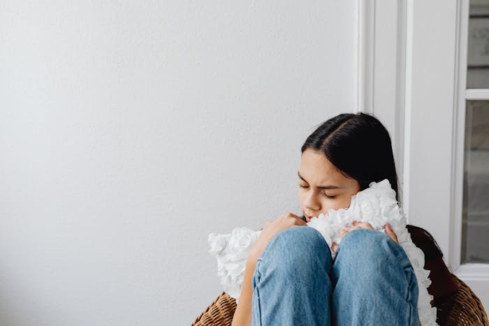 Woman sitting hugging pillow looking sad reflecting on family issues Woman sitting hugging pillow looking sad reflecting on family issues