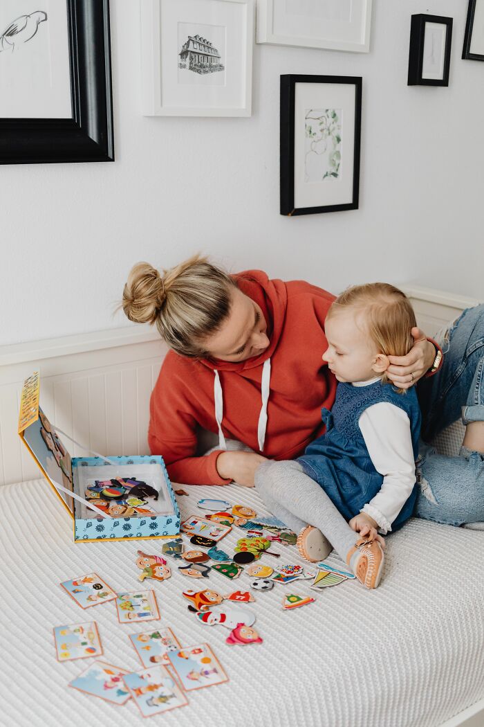 Mother interacting with toddler playing with puzzles on bed