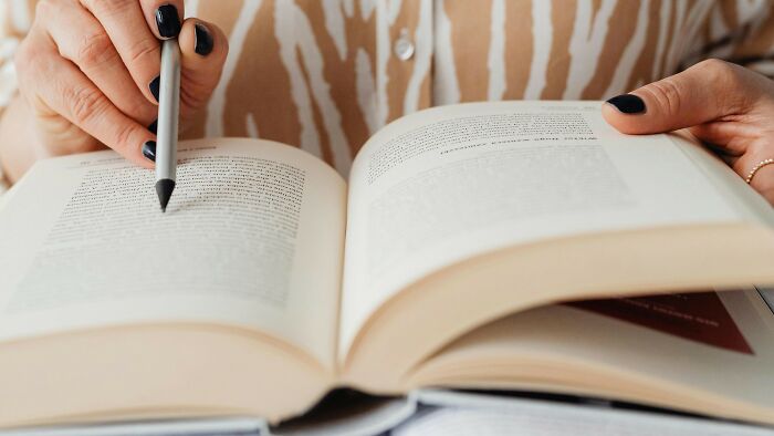 Person studying SAT-level vocabulary words in an open book with a pen in hand Person studying SAT-level vocabulary words in an open book with a pen in hand