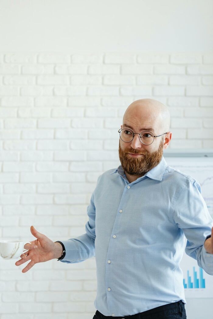 Bald man with beard shrugging while holding a coffee cup representing lazy attitude