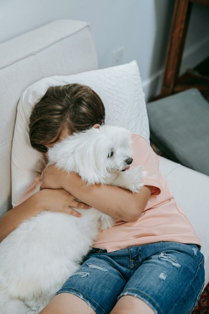 Child hugging a fluffy white dog on bed