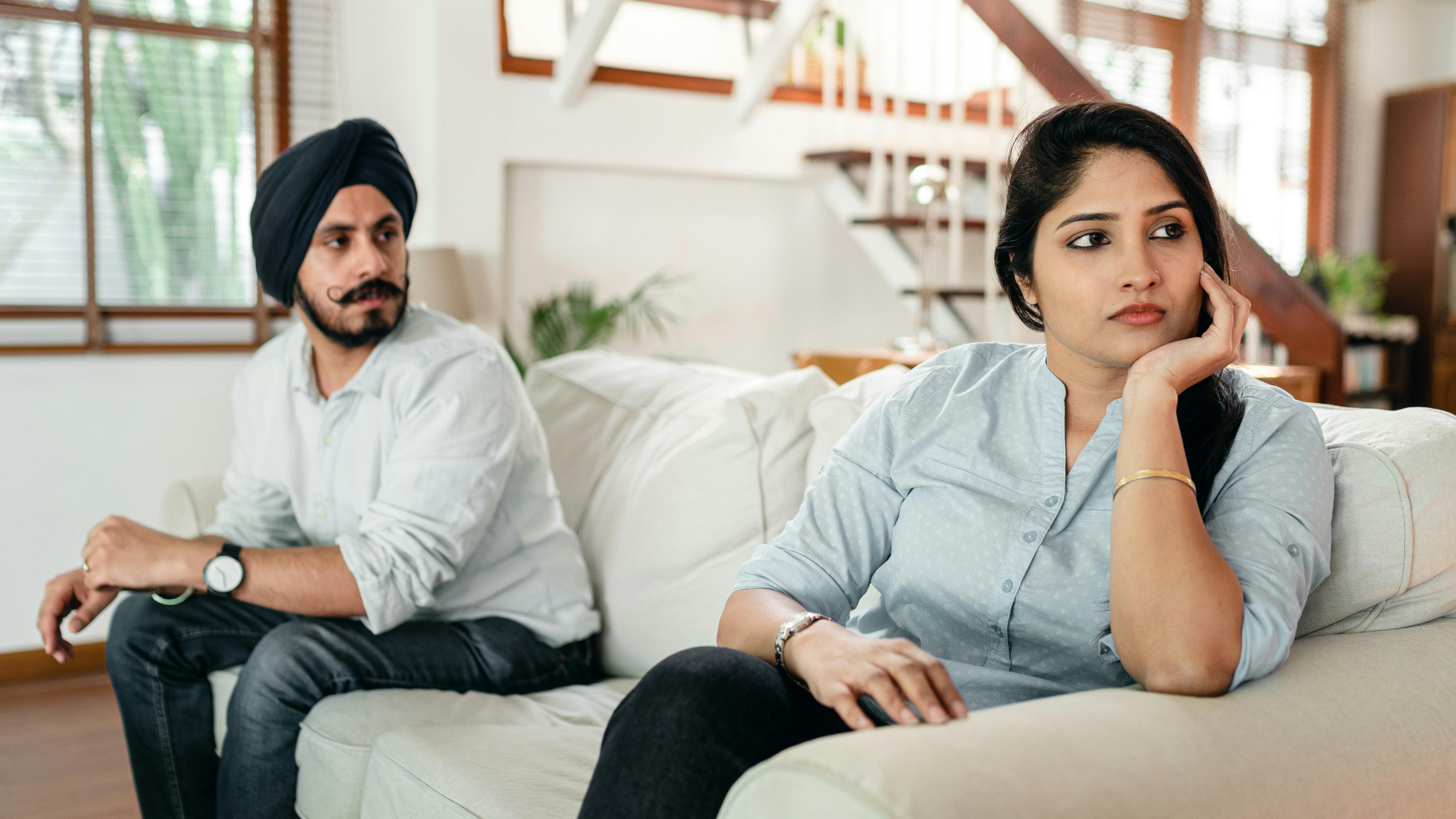 Couple sitting on couch with woman upset and man looking at her Couple sitting on couch with woman upset and man looking at her