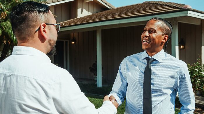 Two men shaking hands outside a house in a friendly neighborhood