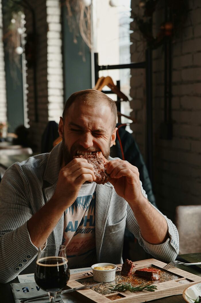 Man enjoying eating steak in rustic restaurant with drink
