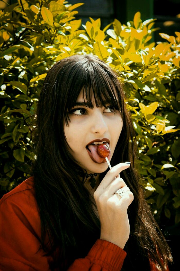 Woman with dark hair licking red lollipop in garden