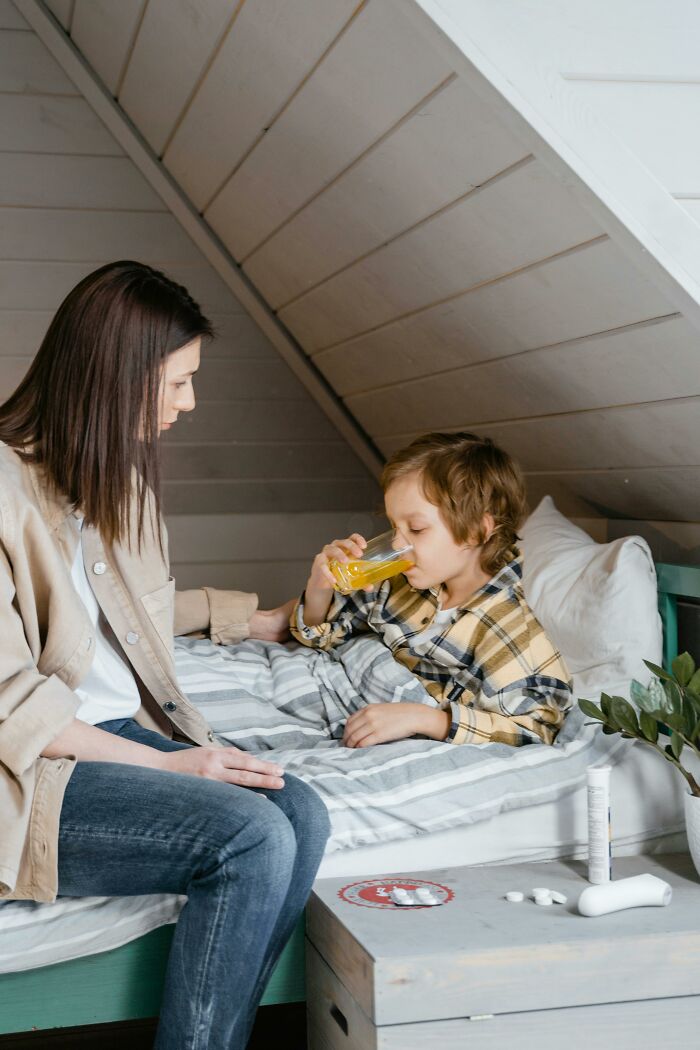 Mother sitting beside sick child drinking orange juice in bed