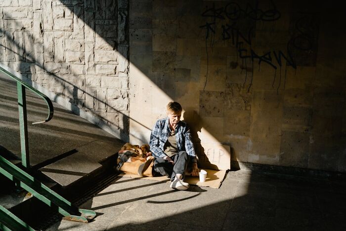 Homeless person sitting in shadow with cardboard sign
