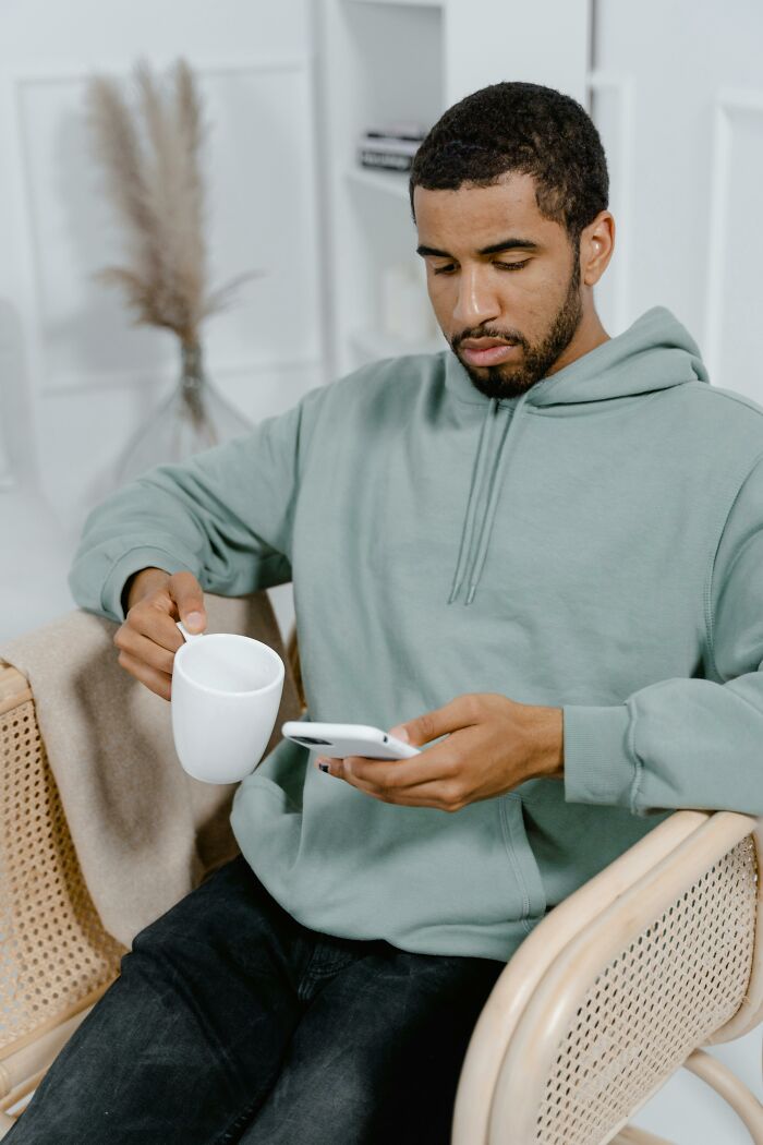 Man in hoodie looking at phone holding mug reflecting on escaping a cult moment