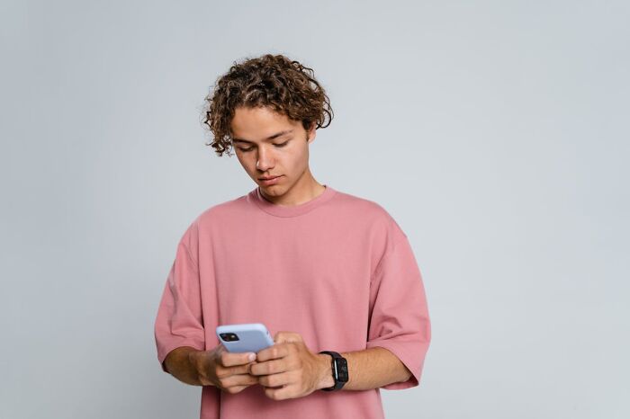 A young man with curly hair in a pink shirt looks down at his phone, experiencing a dumbfounding moment while visiting the US.