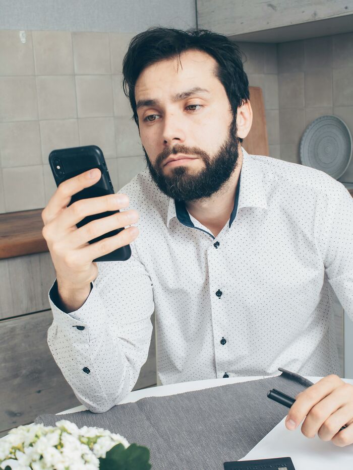 Bearded man looking at phone with a serious expression showing frustration