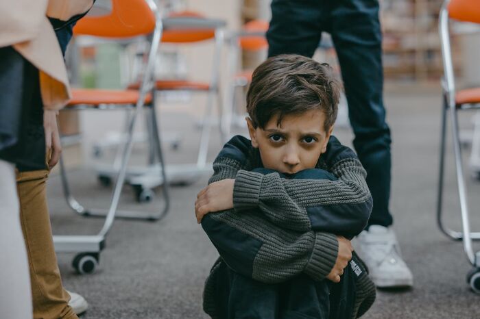 Worried boy sitting on floor in courtroom with adults standing nearby