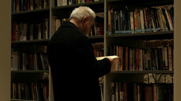 Older man reading book in a dimly lit library focusing on general knowledge facts Older man reading book in a dimly lit library focusing on general knowledge facts