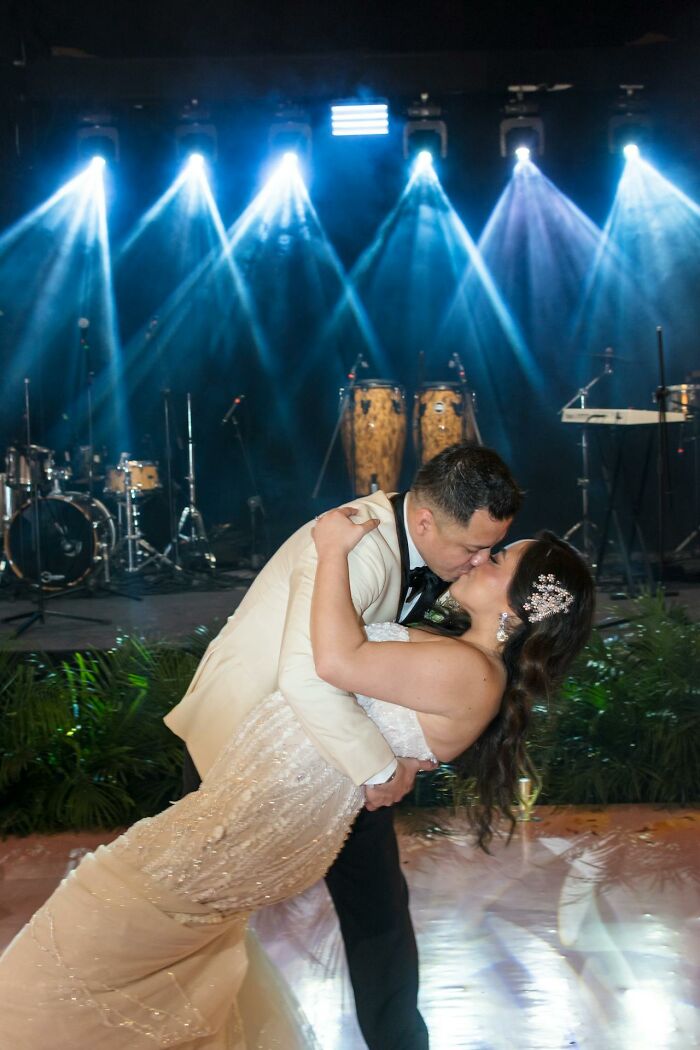 Newlywed couple kissing on the dance floor, illuminated by stage lights during their wedding. Captures a joyous wedding moment.