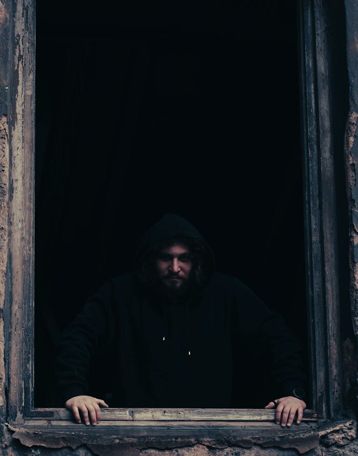 Man with beard staring from dark window frame