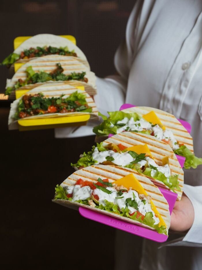 Plated tacos with lettuce, cheese, and sauce stacked in server's hands