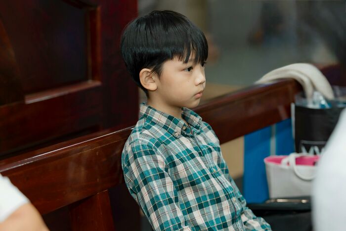 A young Asian boy in a plaid shirt sits on a wooden bench, looking thoughtful, like many lawyers contemplating hard cases.