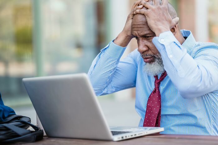 Older generations: Frustrated man with hands on head, looking at laptop. He's struggling to understand Gen Z.