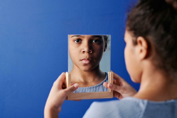Girl looking thoughtfully in a handheld mirror against blue wall