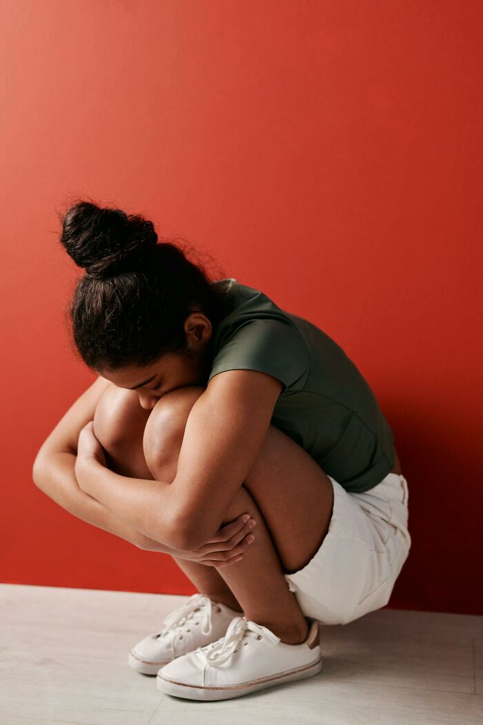 Woman sitting curled up looking sad against red wall