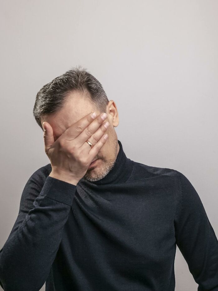 A man in a black turtleneck covers his face with his hand in shame, reflecting deeply immoral things witnessed.