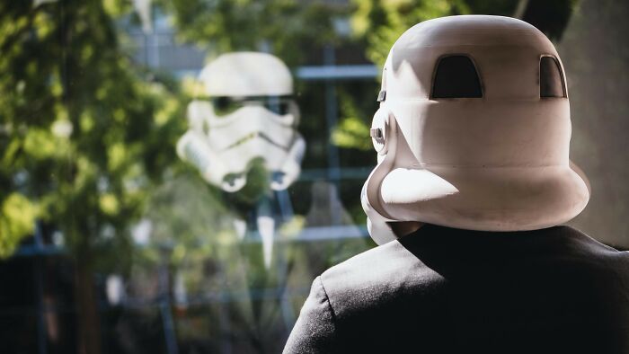 A person in a Stormtrooper helmet looks out a window. A reflection of another Stormtrooper is visible. Guess 15 Films.