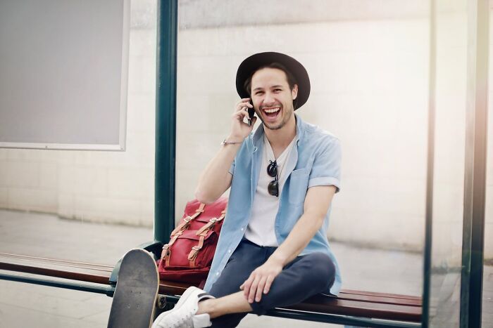 Happy man talking on phone sitting by skateboard showing casual laziness
