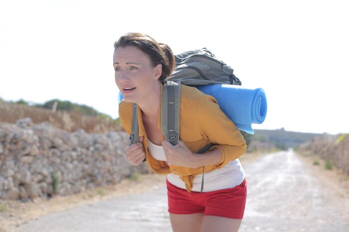 Woman hiking on a dirt road carrying a heavy backpack with a sleeping pad