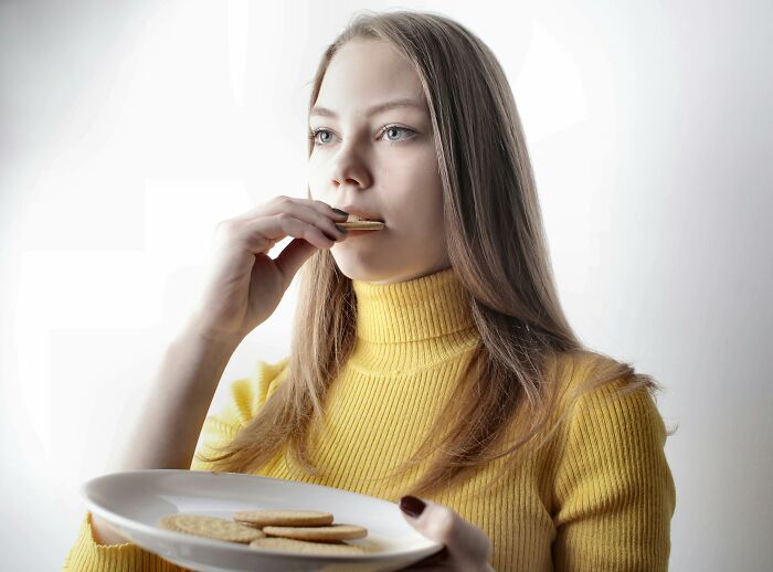 Woman in yellow sweater eating cookie from plate while looking away