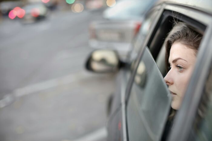 A pensive woman looking out of a car window, hinting at discovery or reflection about partner cheating.