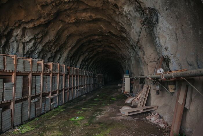 A dark, abandoned tunnel with stacked shelves on the left and debris on the right, evoking disturbing d***h stories.