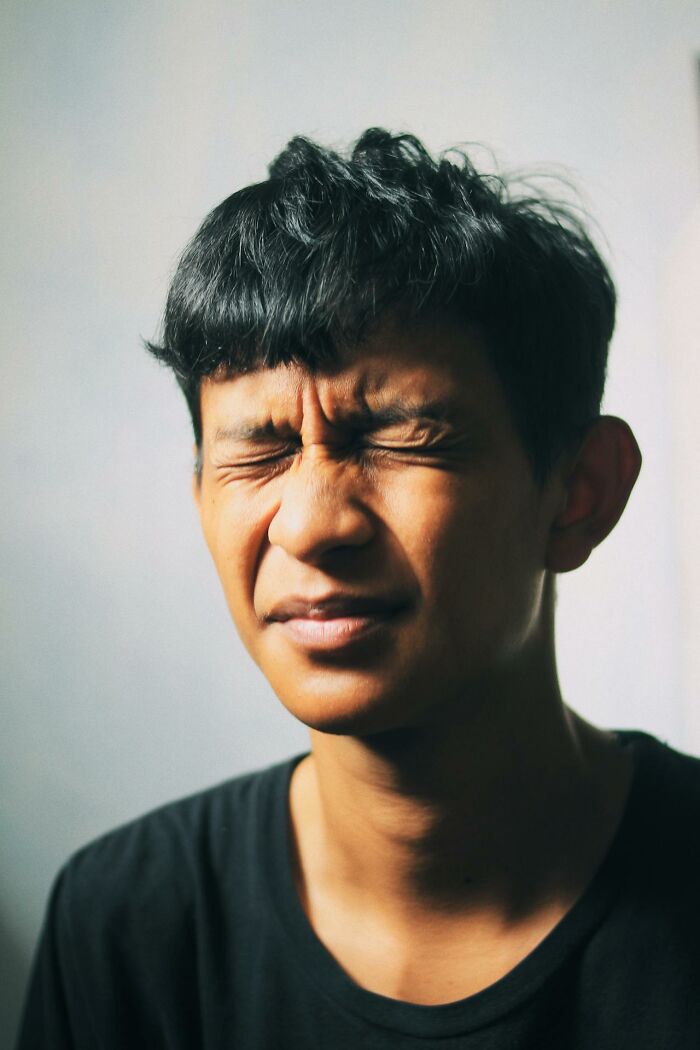 A person with dark hair and a black shirt grimaces, eyes tightly shut, questioning reality amidst a Matrix glitch.