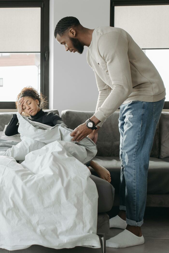 Man caring for a tired woman resting on a couch with a blanket